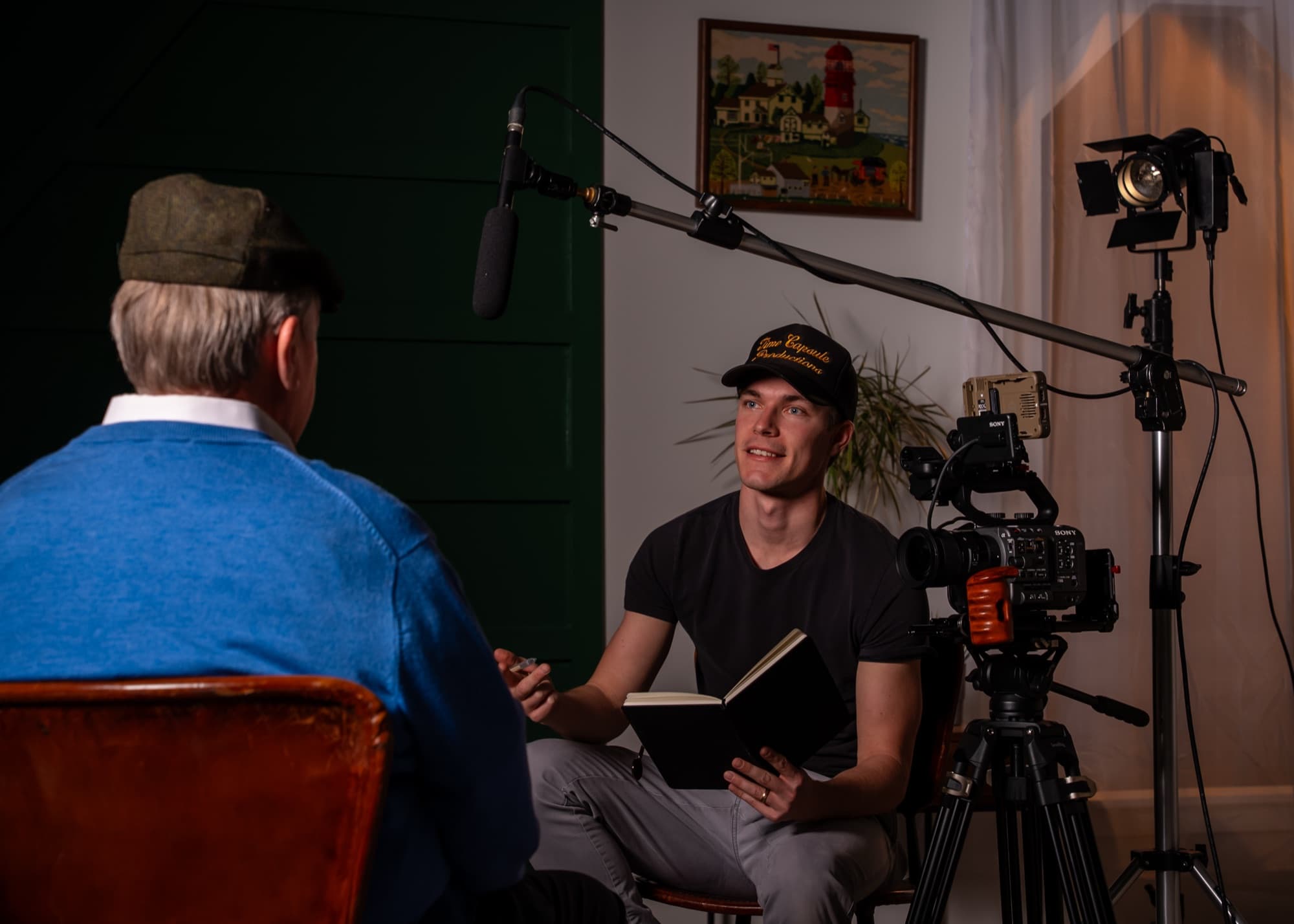 Graham Merten on set with a camera, boom microphone, and lights, interviewing a man